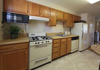 Kitchen with white appliances and wooden cabinets at Foxridge Townhomes, Baltimore, MD